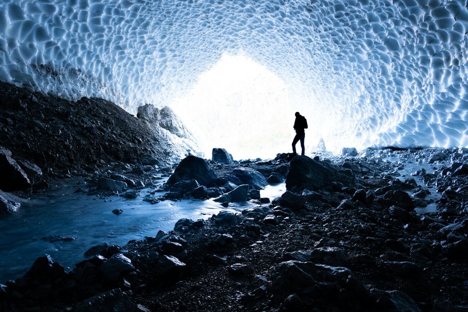 Exploring a stunning ice cave with blue glacial formations and rocky floor.