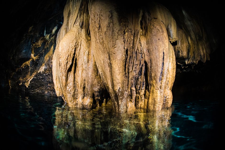 Close-up of stalactites reflecting in water inside a mystical cave setting.